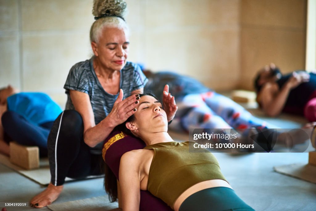 Senior woman performing Reiki o woman in yoga class