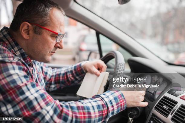 hombre con anteojos revisando su coche y escribiendo cosas al sentarse en el asiento del conductor - kilometer fotografías e imágenes de stock