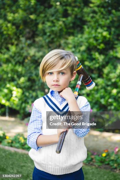 portrait of cute blond boy holding croquet mallet at back yard - lässig schicker stil stock-fotos und bilder