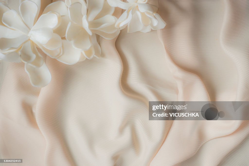 Light beige beautifully draped fabric and white silk flowers. Top view.