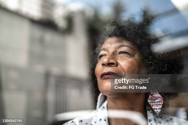 donna anziana che guarda attraverso la finestra di casa - self satisfaction foto e immagini stock