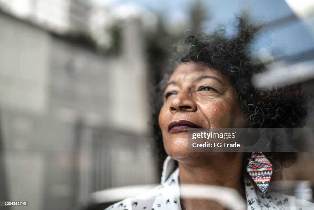 Senior woman looking through the window at home