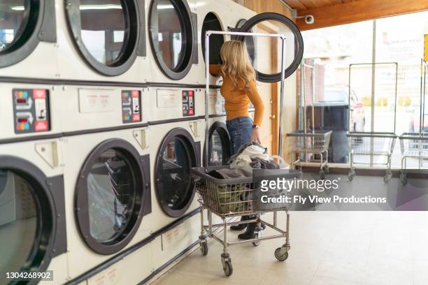 adult woman doing laundry at a laundromat - launderette stock pictures, royalty-free photos & images