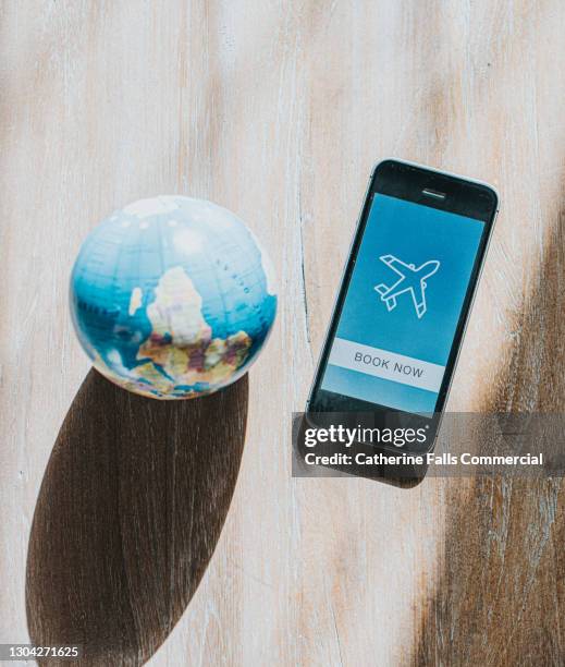 mobile phone displaying an air travel booking app beside a globe - travel cancellation stock pictures, royalty-free photos & images