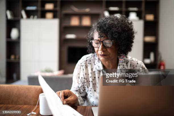 senior woman working from home or using laptop planning or paying bills - investing for retirement imagens e fotografias de stock