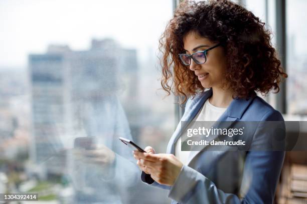 joven empresaria que usa teléfono inteligente en la oficina - banco fotografías e imágenes de stock