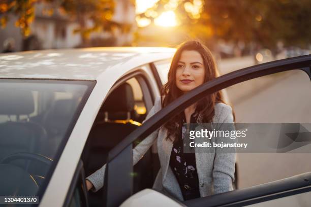 young woman getting into car in town - entering stock pictures, royalty-free photos & images