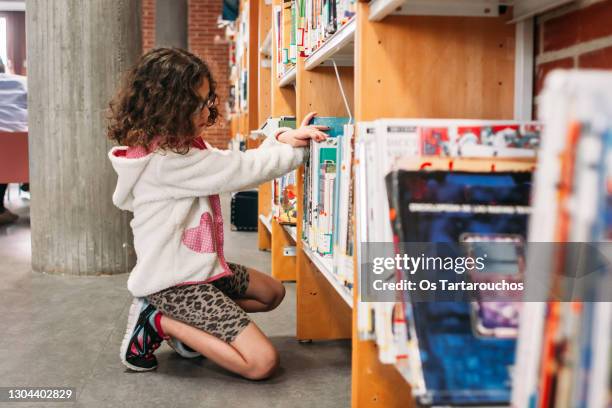 girl choosing books from the shelves of the public library - öffentliche bibliothek stock-fotos und bilder