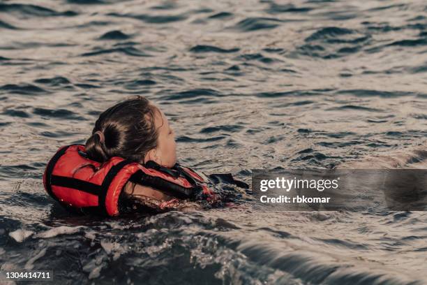 a girl floating in a life jacket faints from hypothermia and drowns in the sea waves after a night shipwreck - schwimmweste stock-fotos und bilder