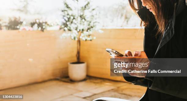 woman grips a mobile phone with two hands and seems serious as she looks down at the screen - spy hunter stock pictures, royalty-free photos & images