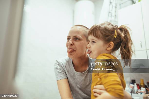 madre con cáncer abrazando a su hija en el baño y haciendo caras. - supervivientes fotografías e imágenes de stock