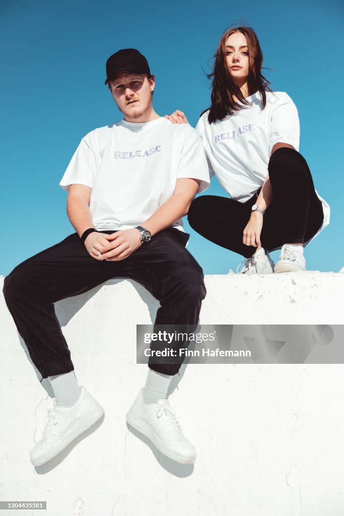 Pareja joven de moda sentada en la pared de hormigón Retrato de moda moderna