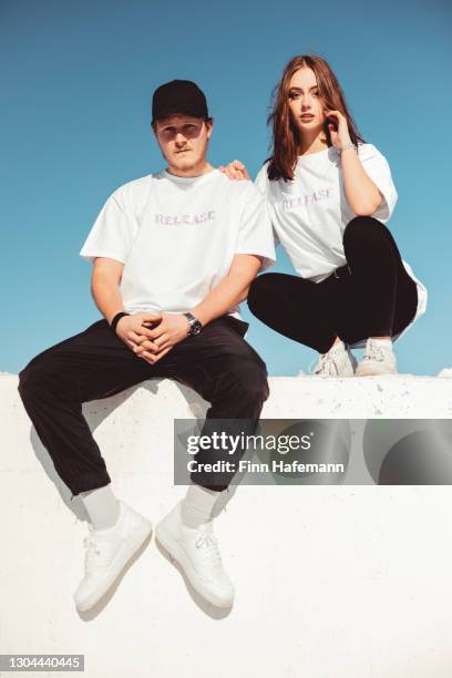 young couple sitting on concrete wall - modern urban fashion portrait - fashion model couple stock pictures, royalty-free photos & images