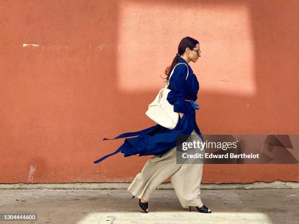 Julia Comil wears sunglasses from Chanel, a blue spring trench coat from Nehera, beige linen flared pants from Nehera, a large triangle-shaped white...