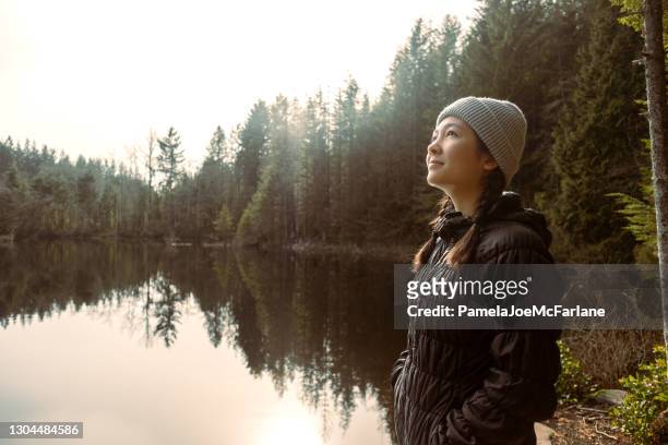 multi-ethnic young woman in quiet contemplation at edge of lake - vancouver canada stock pictures, royalty-free photos & images