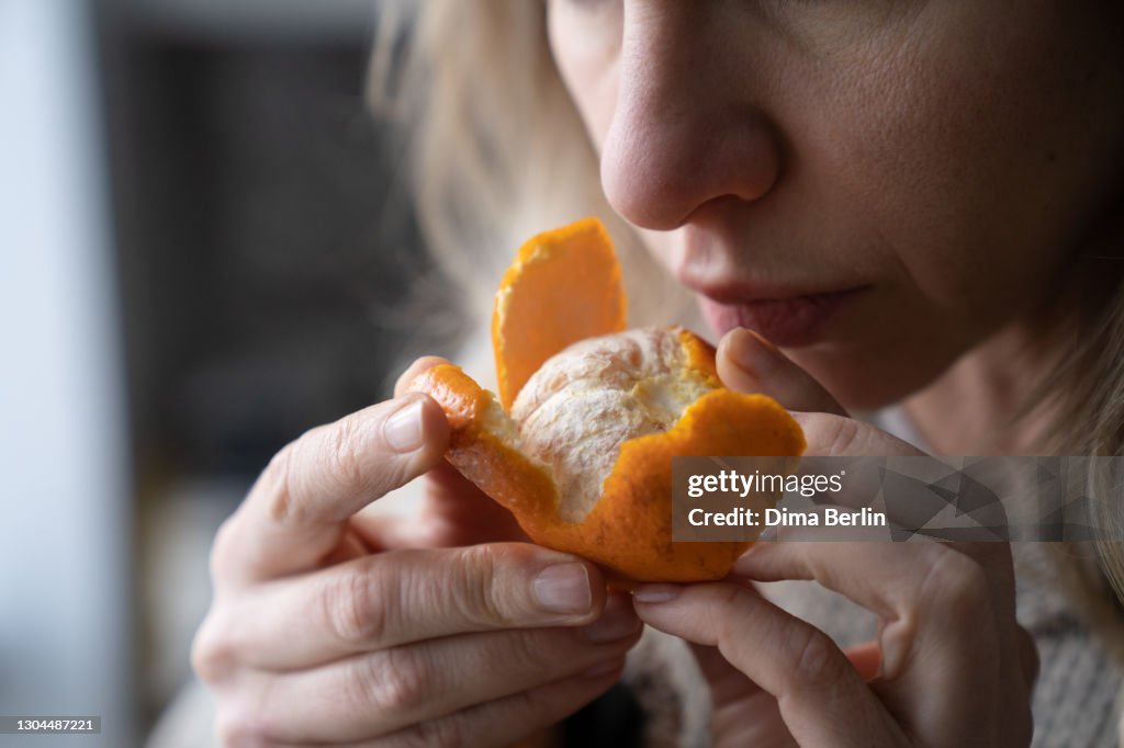 Sick woman trying to sense smell of fresh tangerine orange, has symptoms of Covid-19, corona virus