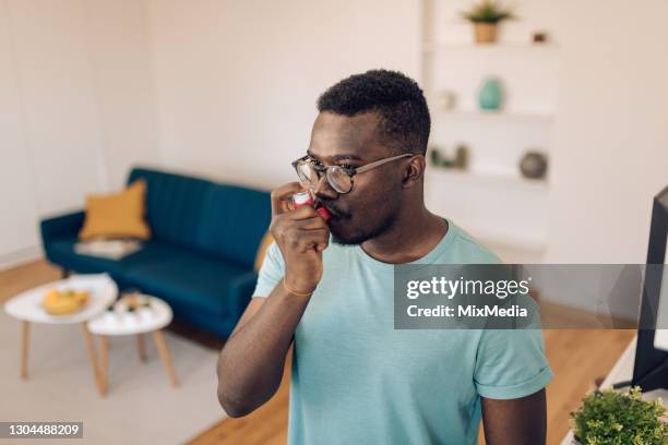 young man using asthma inhaler at home - inhaler stock pictures, royalty-free photos & images