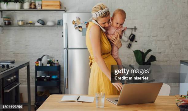 eine junge lächelnde geschäftsfrau, die einen telefonanruf hat, während sie ihr baby-mädchen zu hause hält - busy mom stock-fotos und bilder