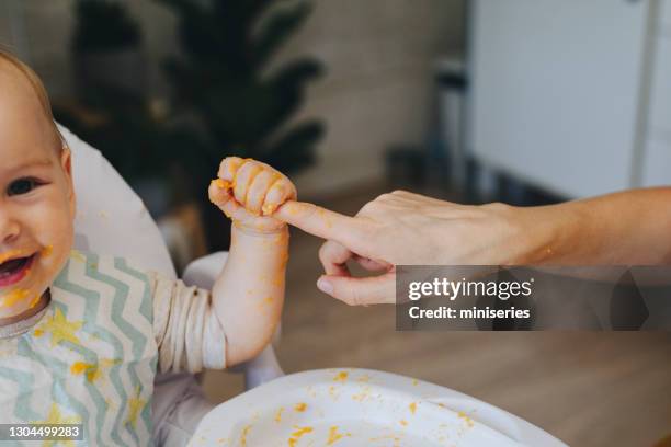 ein entzückendes lächelndes baby mädchen, das den finger ihrer mutter zu hause hält - baby spielt mit essen stock-fotos und bilder