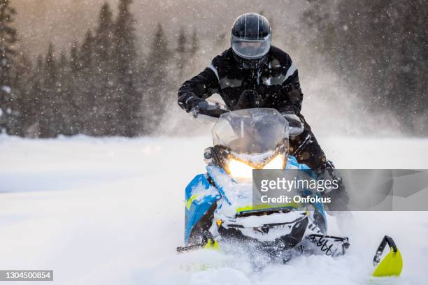 man having fun speeding with a snowmobile through the powder snow at sunset - snow vehicle stock pictures, royalty-free photos & images