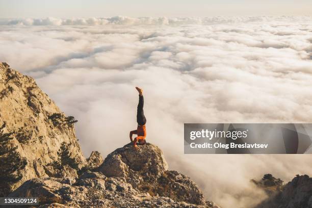 man practicing hatha yoga in headstand (salamba shirshasana) position in mountains with amazing view of low clouds at sunset - shirshasana stock pictures, royalty-free photos & images