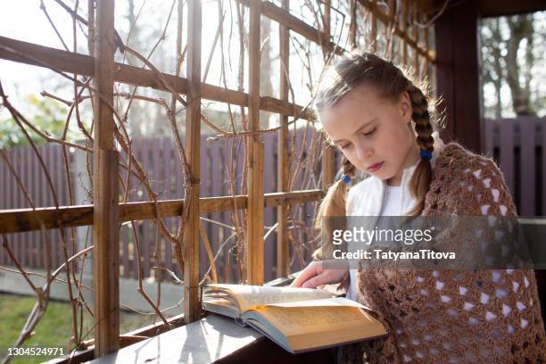 a girl with braids is reading an analog book in nature, in garden house - grid girls foto e immagini stock