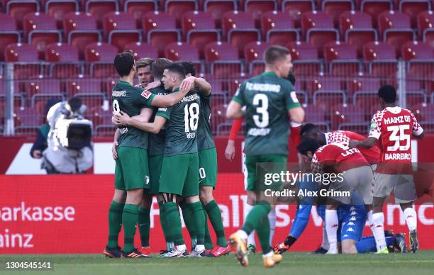 Andre Hahn of FC Augsburg celebrates with team mates after scoring their side's first goal as 1. FSV Mainz players console team mate Robin Zentner...