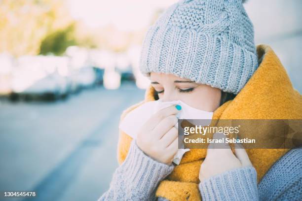 close up view of a young caucasian woman dressed in winter clothing as she blows her nose from being ill. - cachecol imagens e fotografias de stock