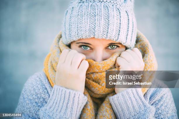 front view of a young blue-eyed caucasian woman covering half her face with a scarf and staring into the camera. - woman face hat foto e immagini stock