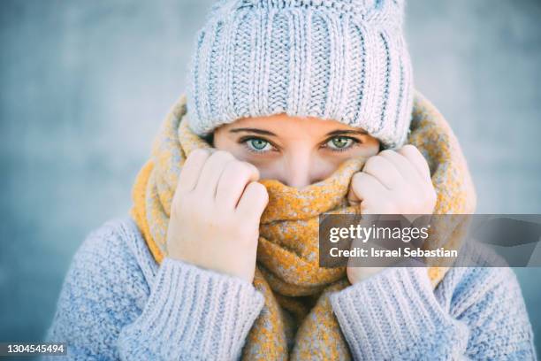 front view of a young blue-eyed caucasian woman covering half her face with a scarf and staring into the camera. - winter health imagens e fotografias de stock