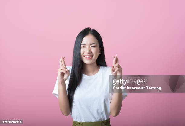 hoping young attractive dark haired woman with casual hairstyle raising hands with crossed fingers while looking worringly at camera, isolated over pink background - woman waist up isolated stock pictures, royalty-free photos & images