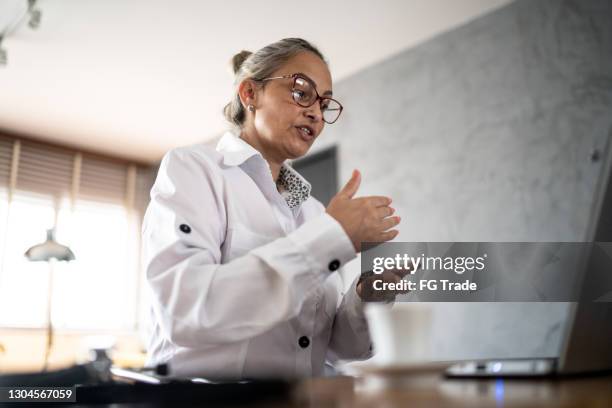 mature female doctor using laptop on a telemedicine call at home - virtual visit stock pictures, royalty-free photos & images