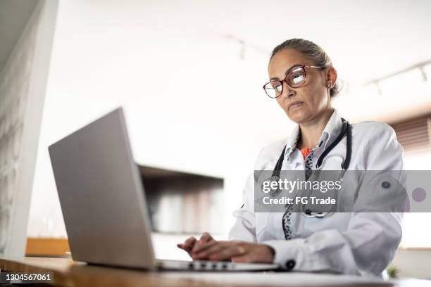 mature doctor working using laptop at home - doctor using laptop stock pictures, royalty-free photos & images