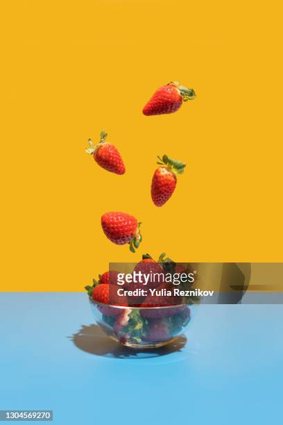 strawberries flying in the bowl on the blue-yellow background - strawberry stock pictures, royalty-free photos & images