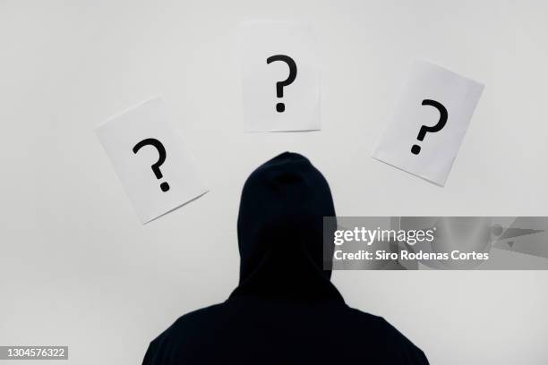 man in hooded jacket looking at question marks on white paper - manquestionmark stock pictures, royalty-free photos & images