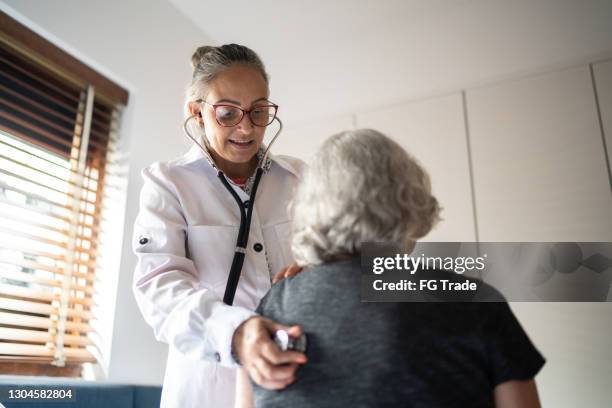 arzt mit stethoskop, um seniorin zu hause zu prüfen - adult patient with doctor and stethoscope stock-fotos und bilder