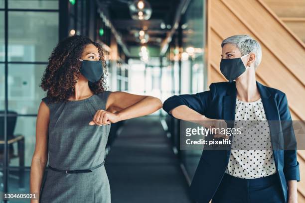 兩個戴著面具的女商人做肘部顛簸 - 碰肘問候 個照片及圖片檔