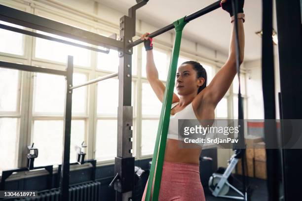 young fit woman doing resistance band assisted pull-ups in gym - chin ups stock pictures, royalty-free photos & images
