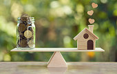 House mortgage and family financial management concept: Wooden home and heart, Family member and US dollar hessian bags on balance scale. Prepare expenses for the purchase of a residence.