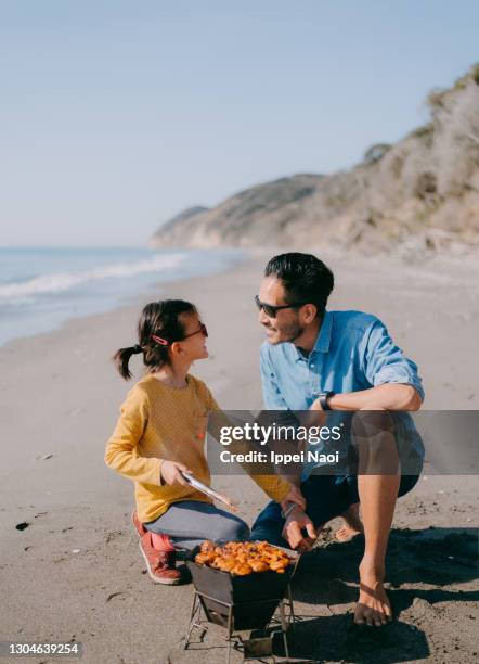 father and young daughter cooking meat on bbq on beach - chiba prefectuur stockfoto's en -beelden
