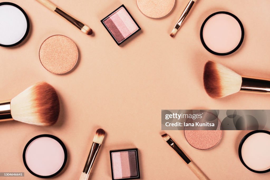 Set of different makeup accessories on beige, brown background. Cosmetic products for skin care. Eyeshadow, blush, face powder, brushes. Copy space.