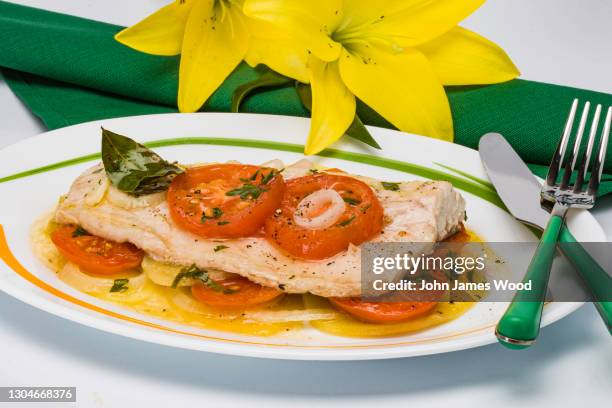 baked merluza fish with tomatoes & sauce in table setting - merluza stockfoto's en -beelden