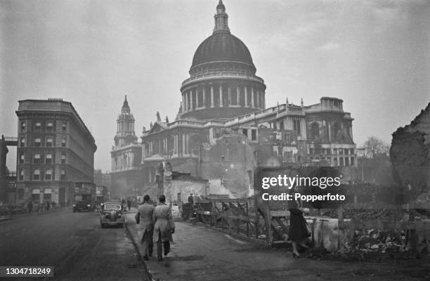 Buses, cars and pedestrians drive and walk along St Paul's Churchyard and Cannon Street beside Blitz damaged bomb sites in front of St Paul's...