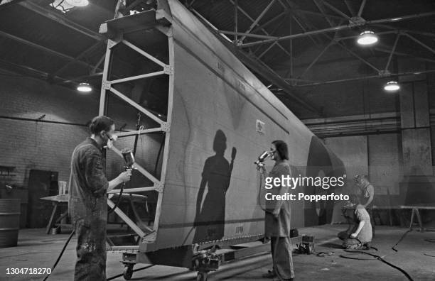 Aircraft workers use spray guns to paint camouflage finish on to the outer section of the main wing of an Avro Lancaster heavy bomber under...