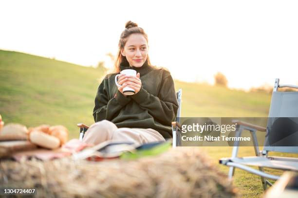 women enjoying coffee or hot drink while sitting on camping chair during sunrise. camping, simple, sustainable lifestyle. - camping chair stock pictures, royalty-free photos & images