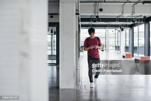 student walking at hallway texting on his mobile phone - a teen thai stock pictures, royalty-free photos & images