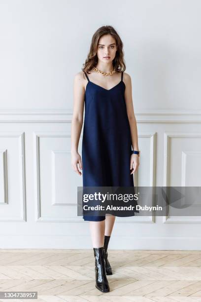 young woman in a dress looking at the camera against a background of a white wall - blue dress fotografías e imágenes de stock