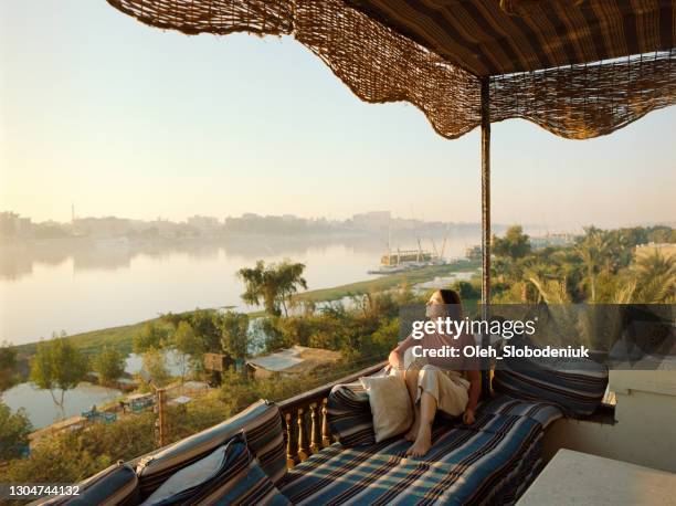 femme s’asseyant sur la terrasse et regardant le nil au coucher du soleil dans louxor - louxor photos et images de collection