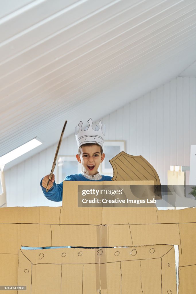 Little boy playing with a cardboard castle and armor at home.
