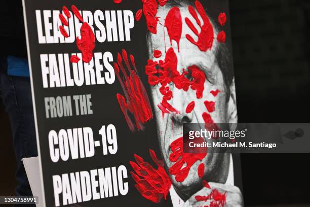 Poster of Gov. Andrew Cuomo's book is seen covered in red painted hands as people gather outside of his NYC office to protest against cuts to health...